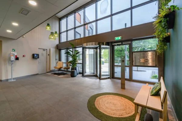 Moderne en gastvrije entreehal aan de Baarnsche Dijk met glazen draaideur, zithoek en planten.